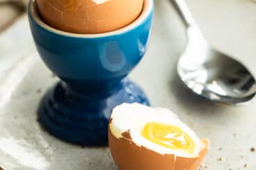 A soft boiled egg in a blue egg cup with toast sticks next to it.