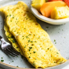 An omelet on a gray plate with a side of fruit.