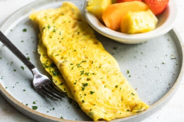 An omelet on a gray plate with a side of fruit.