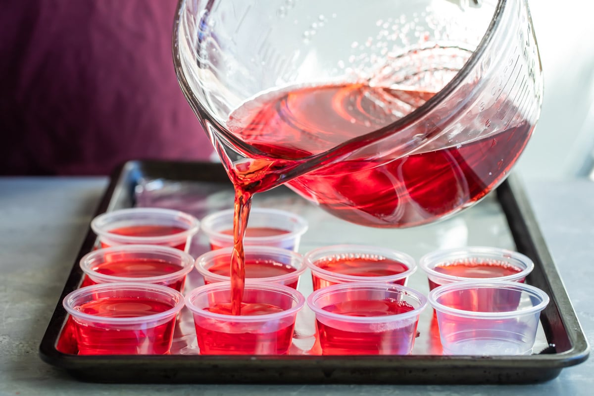 Pouring red jello shots into small cups.