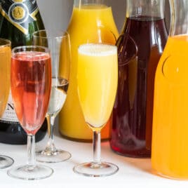 Three carafes with various juices and 4 champagne flutes with mimosas.