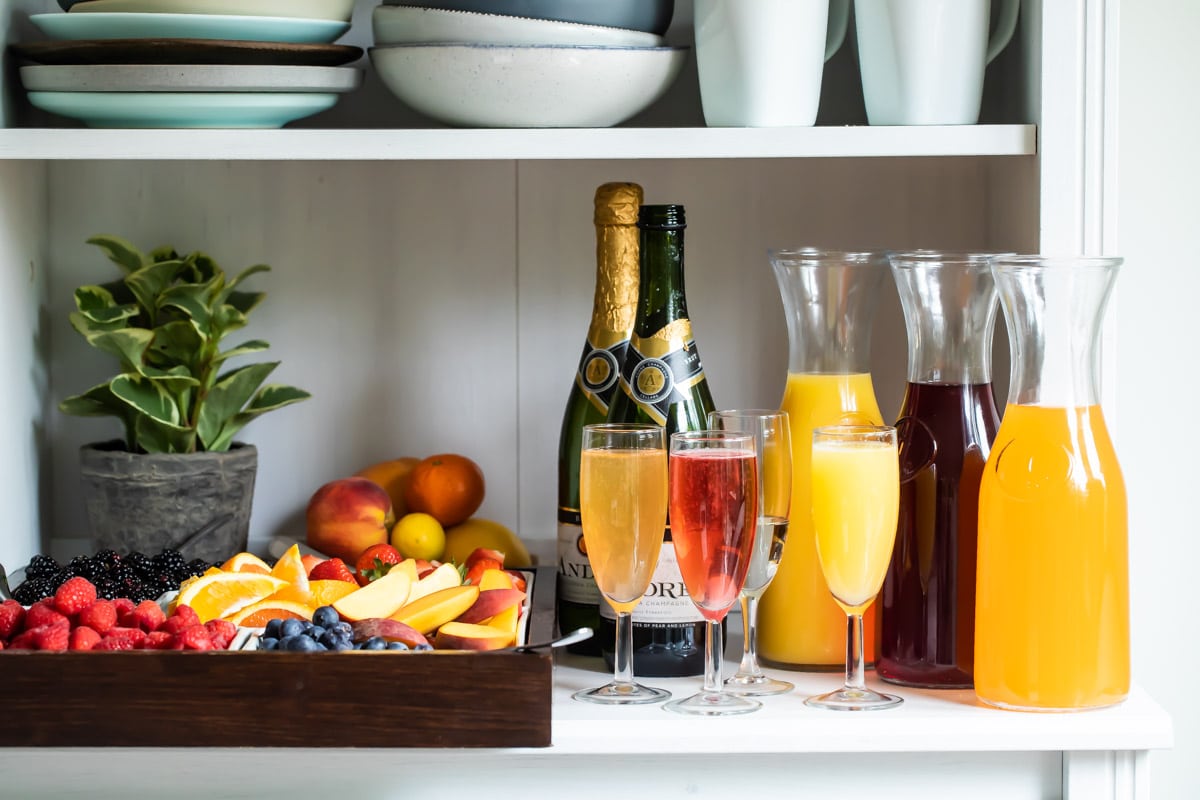 Carafes of juice, bottles of sparkling wine, and fresh fruit garnishes for a mimosa bar.