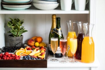 Carafes of juice, bottles of sparkling wine, and fresh fruit garnishes for a mimosa bar.