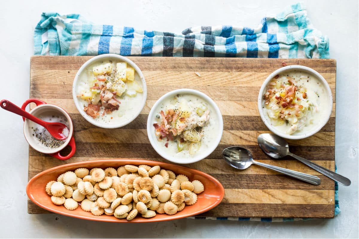 New England clam chowder in white bowls on a wooden cutting board.