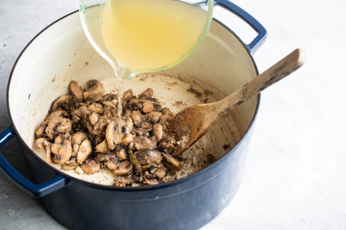 Adding chicken broth to cooked mushrooms.