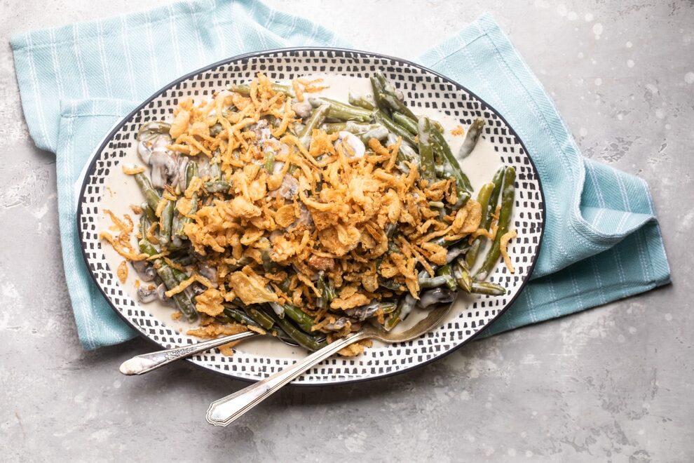 Slow cooker green bean casserole on a black and white serving platter with a serving spoon and fork.