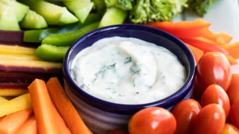 Veggie dip in a small navy blue bowl surrounded by vegetables.