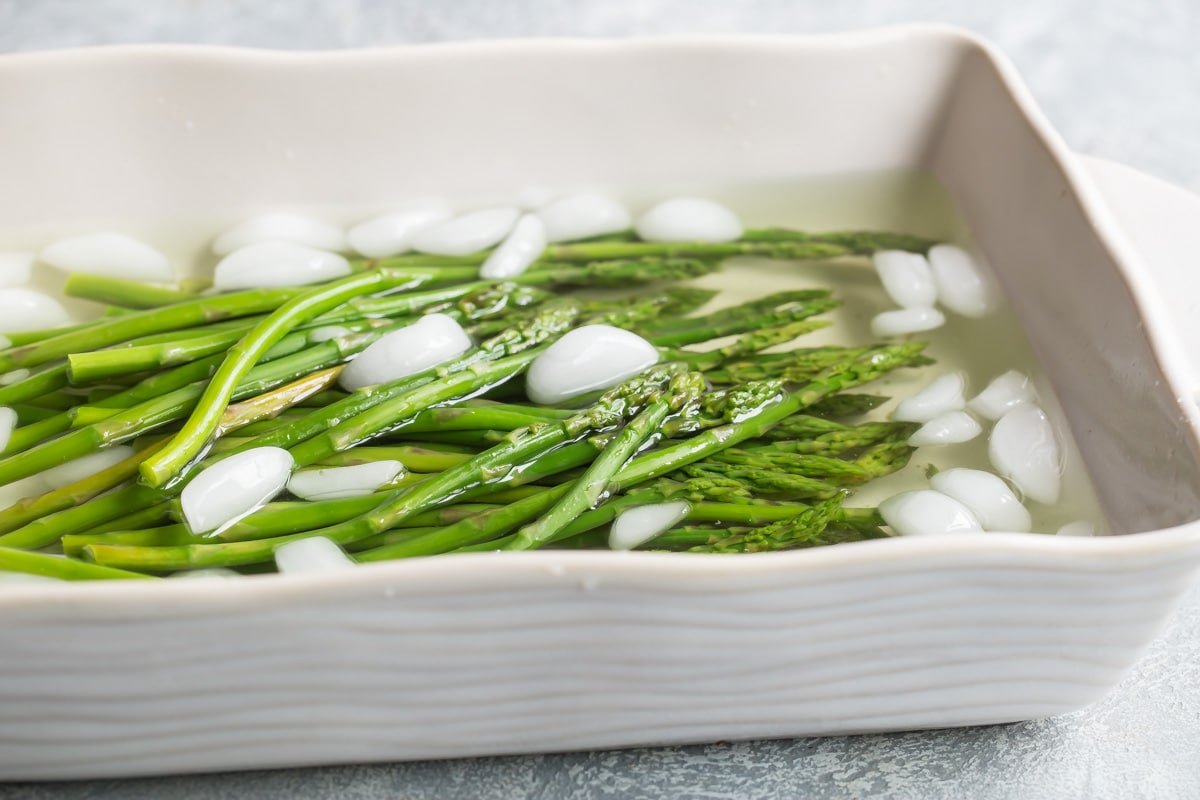 Asparagus in a white dish filled with water and ice.