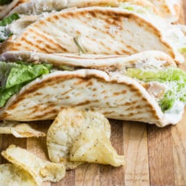 Grilled chicken Caesar wraps on a wood cutting board with chips.