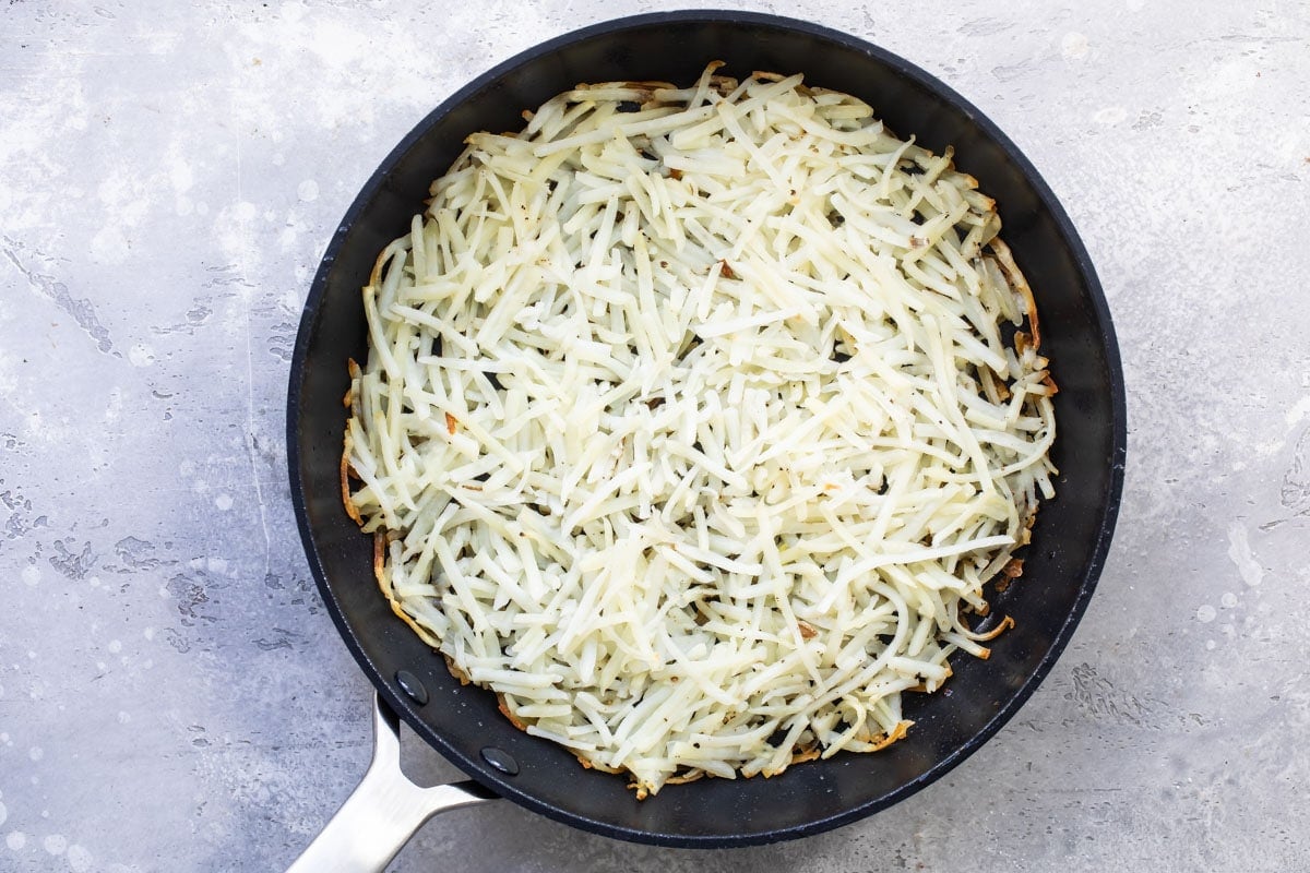 Hash browns cooking in a skillet.