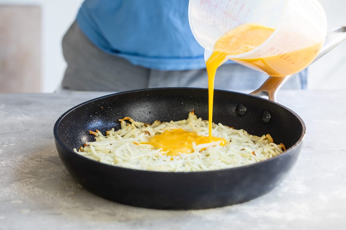 Adding eggs to hash browns in a skillet.