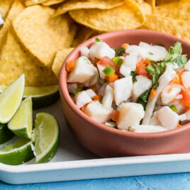 Taliapa ceviche in a pink bowl on a white platter with tortilla chips.