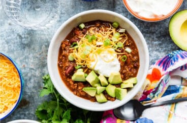 A bowl of turkey chili garnished with cheese, sour cream, scallions, and avocado.