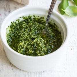 A bowl of pesto with a spoon in it.