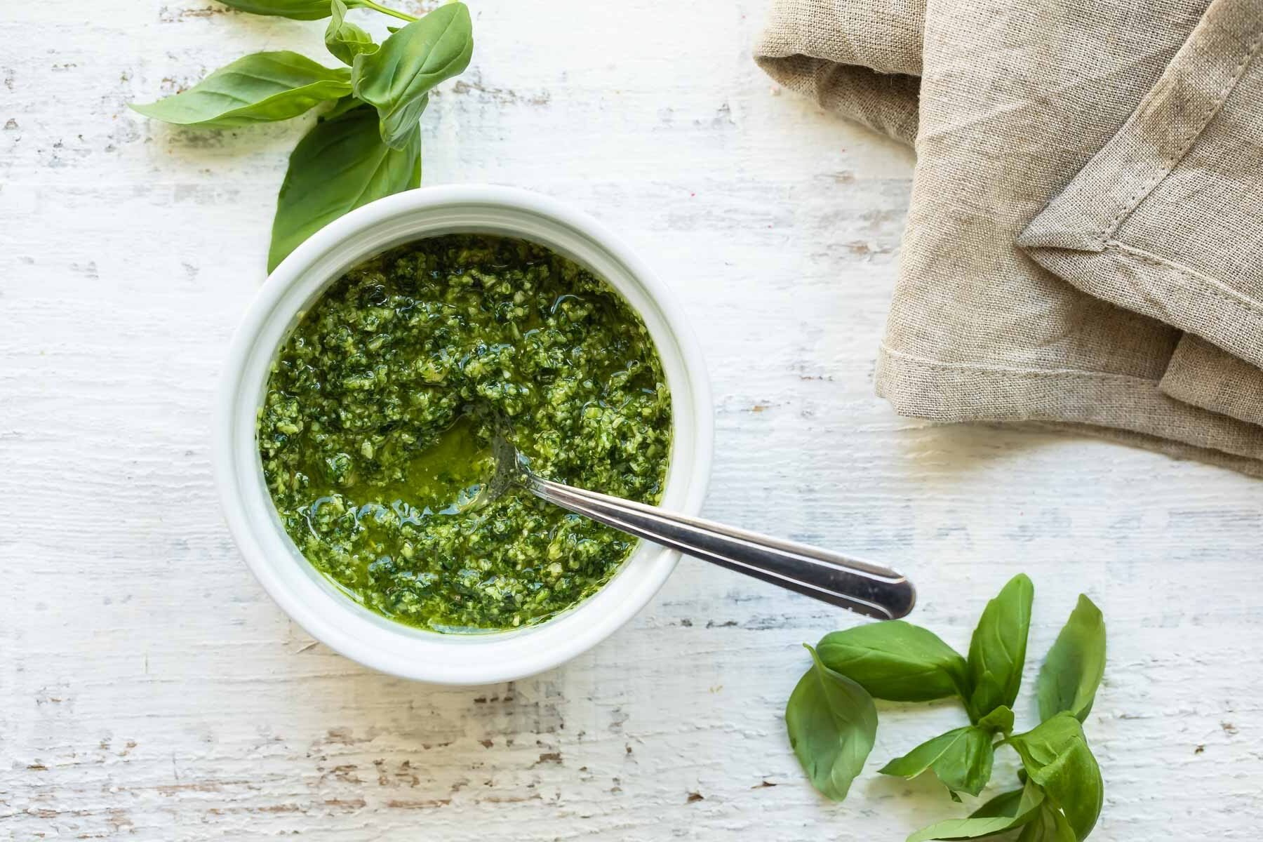 A bowl of pesto with a spoon in it.
