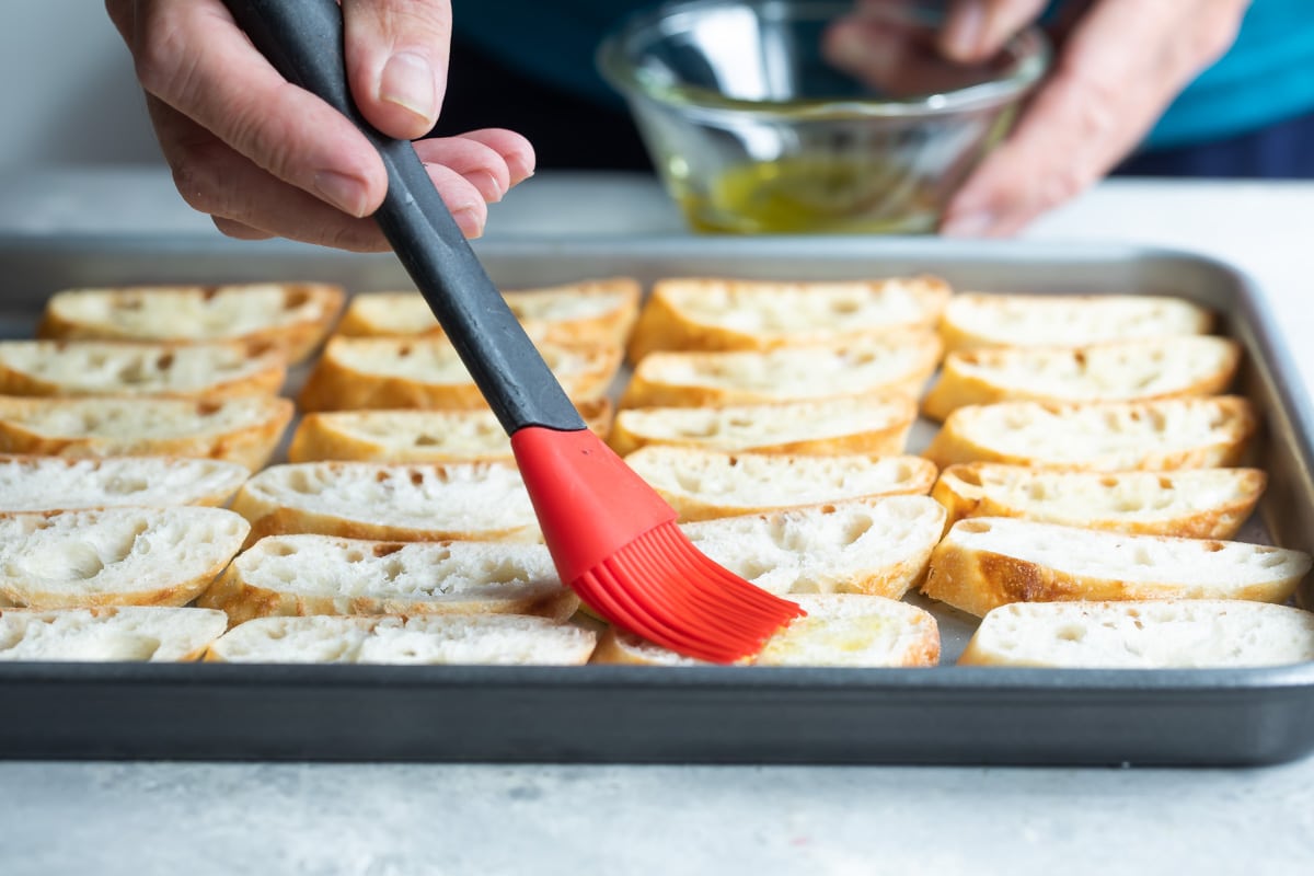 Someone brushing oil on pieces of bread before baking.