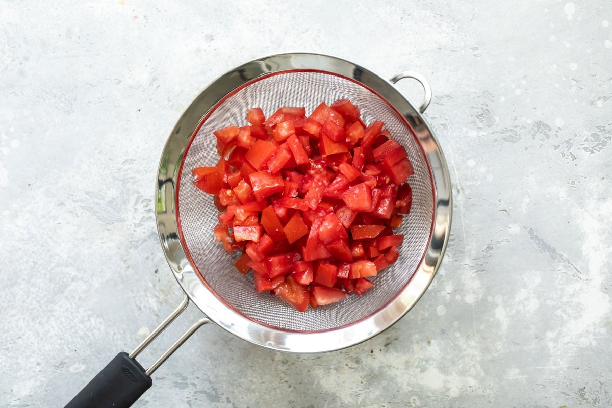 Tomatoes being drained through a sieve.