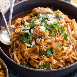 Chicken tinga in a bowl with tortilla shells and lettuce nearby.