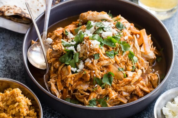 Chicken tinga in a bowl with tortilla shells and lettuce nearby.