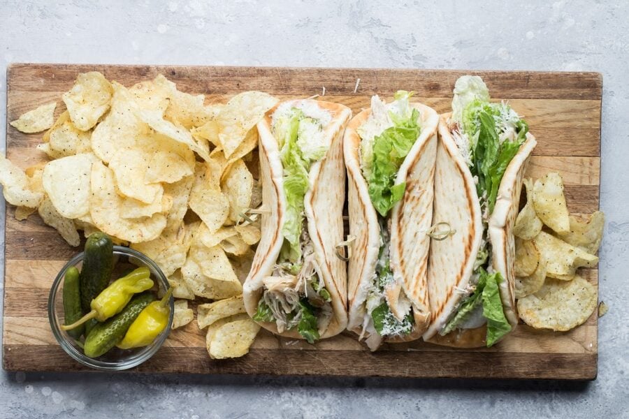 Grilled chicken Caesar wraps on a wood cutting board with chips.