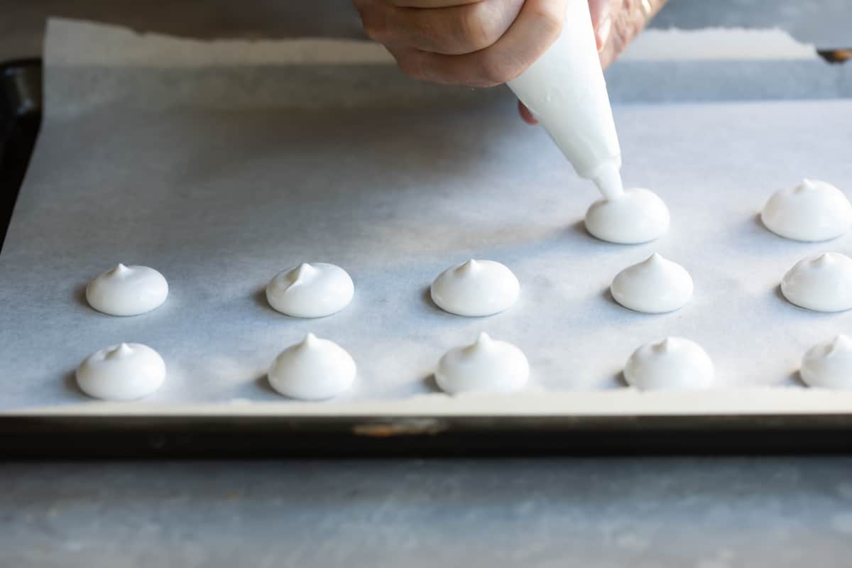 Piping meringue mushrooms on a baking sheet.
