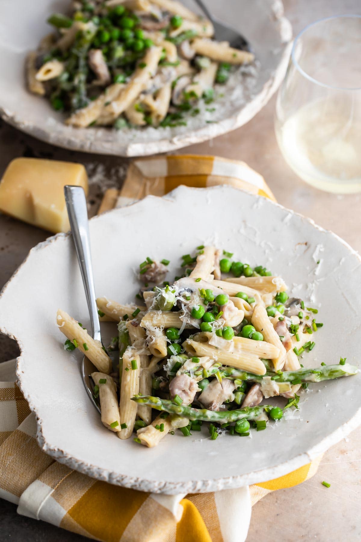 Pasta with peas and prosciutto on two plates with a glass of white wine.