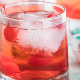 Shirley temples in three clear glasses with a clear bowl filled with cherries.