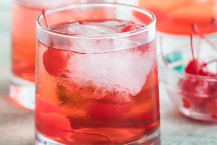 Shirley temples in three clear glasses with a clear bowl filled with cherries.