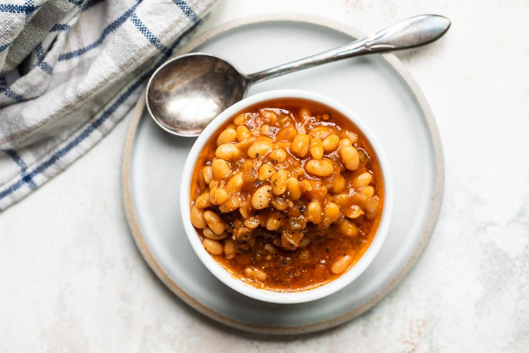 Slow cooker baked beans in a small white bowl.