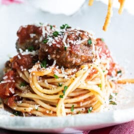 Someone rolling spaghetti noodles on a fork over a plate of spaghetti and meatballs.