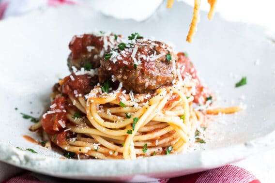 Someone rolling spaghetti noodles on a fork over a plate of spaghetti and meatballs.