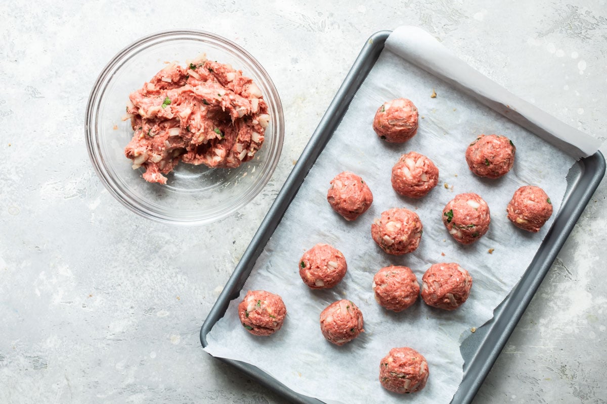 Uncooked meatballs on a parchment paper lined baking sheet.