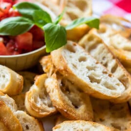 Toasted baguettes on a white platter with bruschetta.