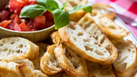 Toasted baguettes on a white platter with bruschetta.