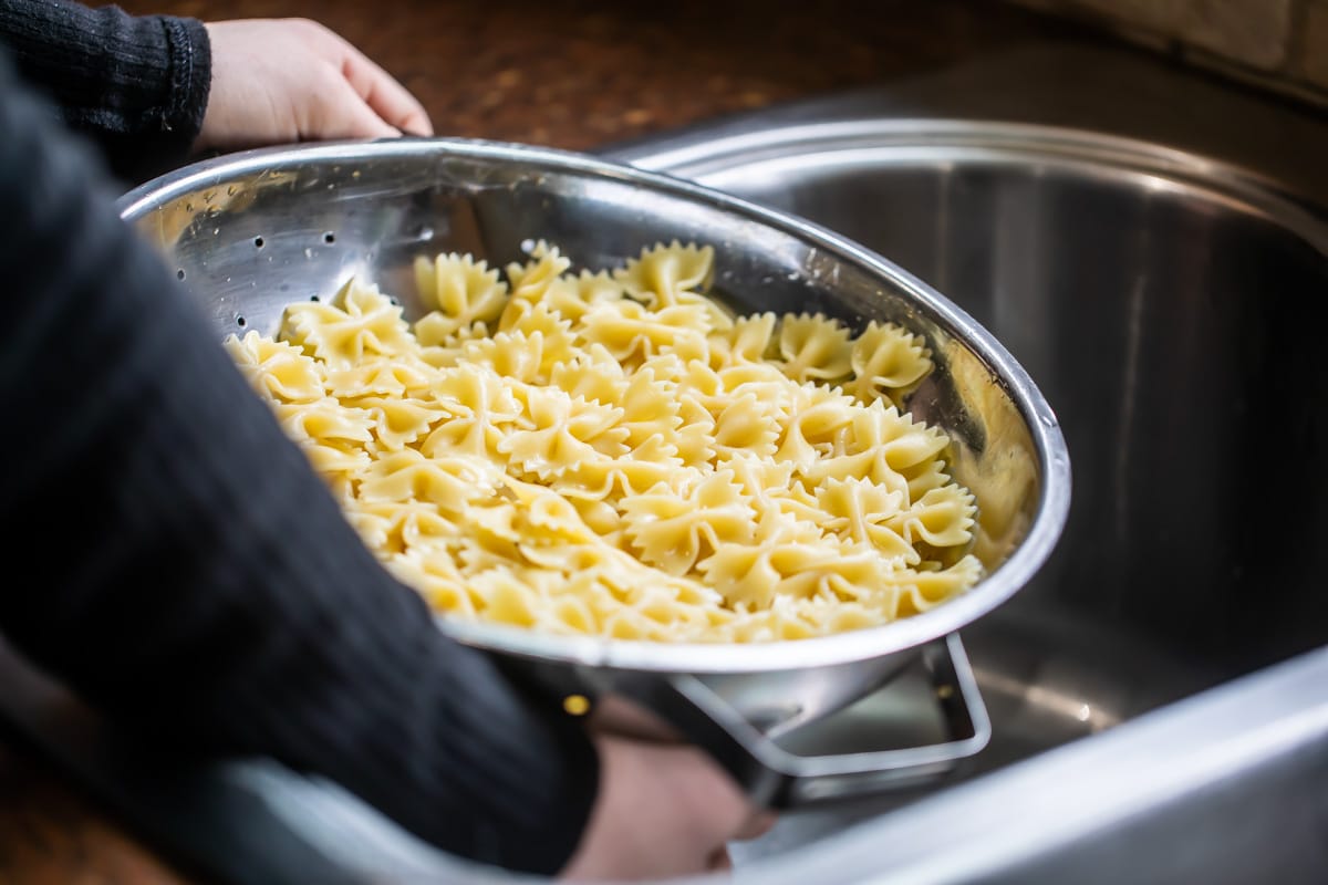 A colander filled with cooked bow tie pasta.