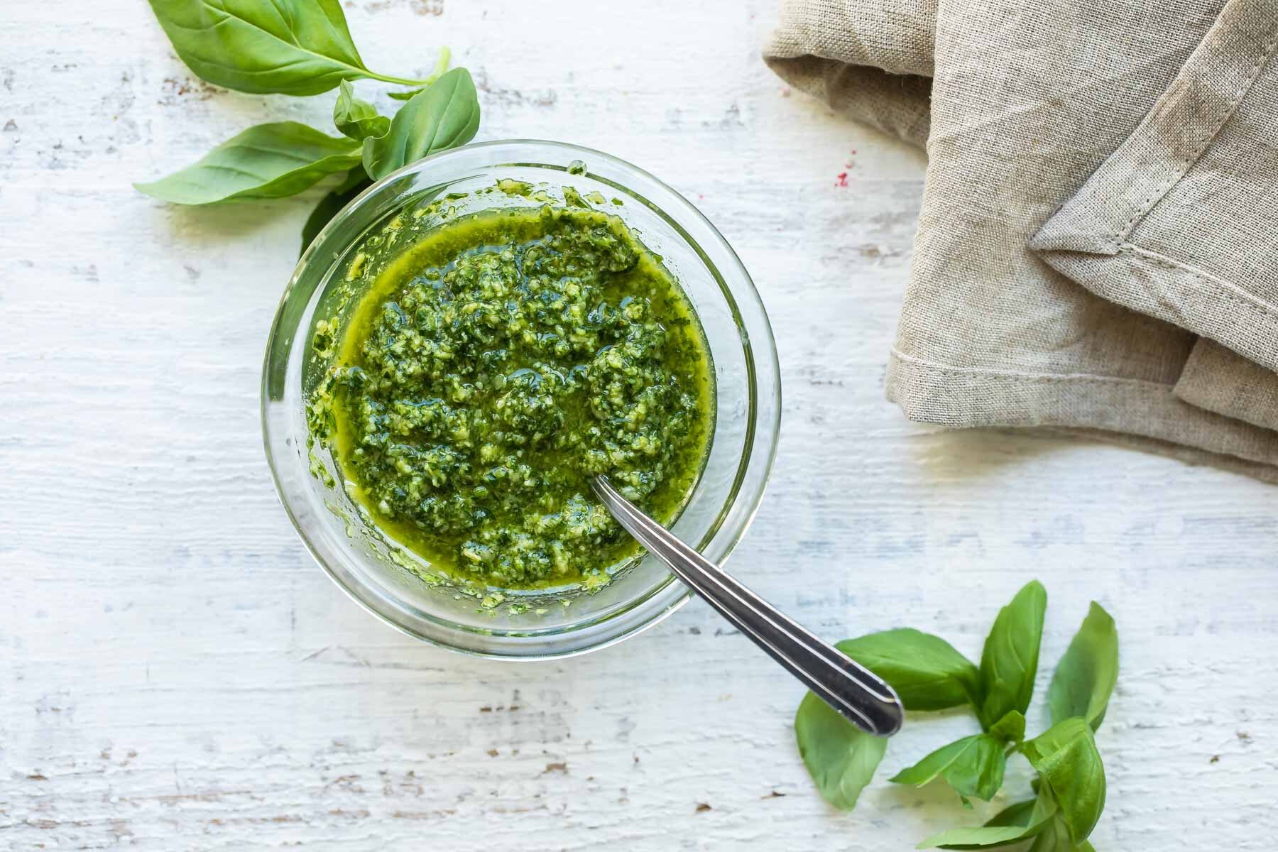 Basil pesto in a silver bowl with a spoon resting in it.