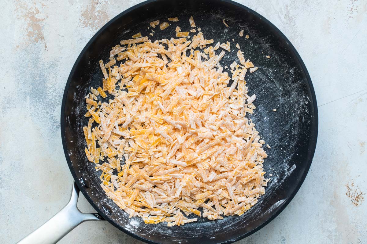 Shredded cheese tossed with cornstarch in a saucepan.