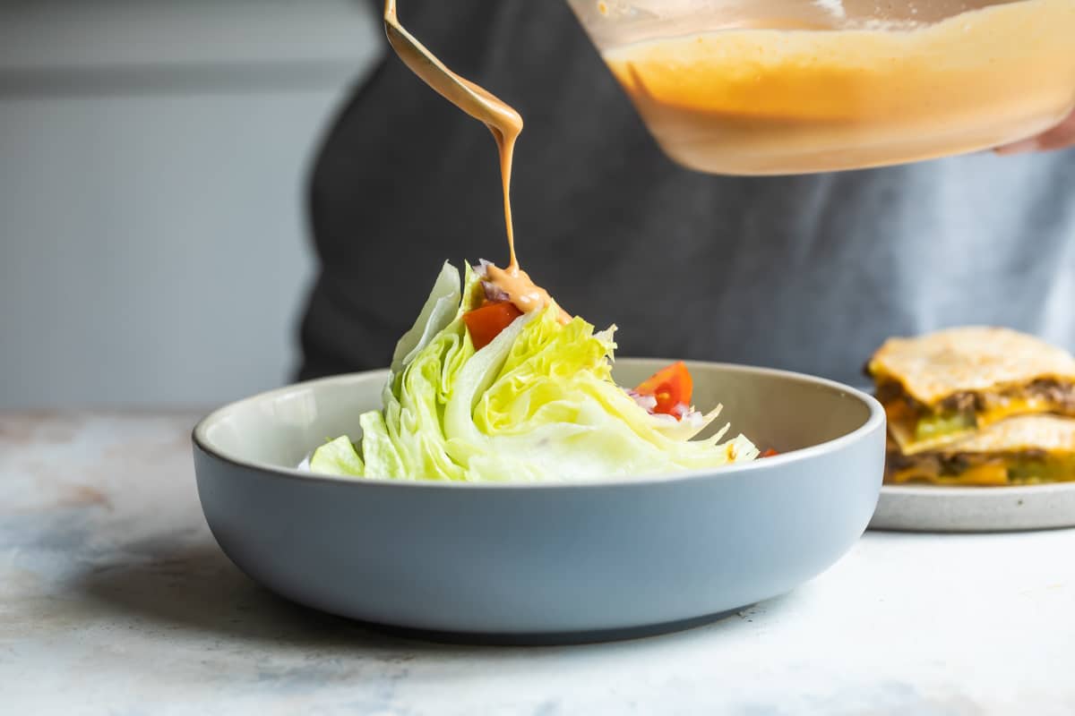 A wedge salad being drizzled with salad dressing.