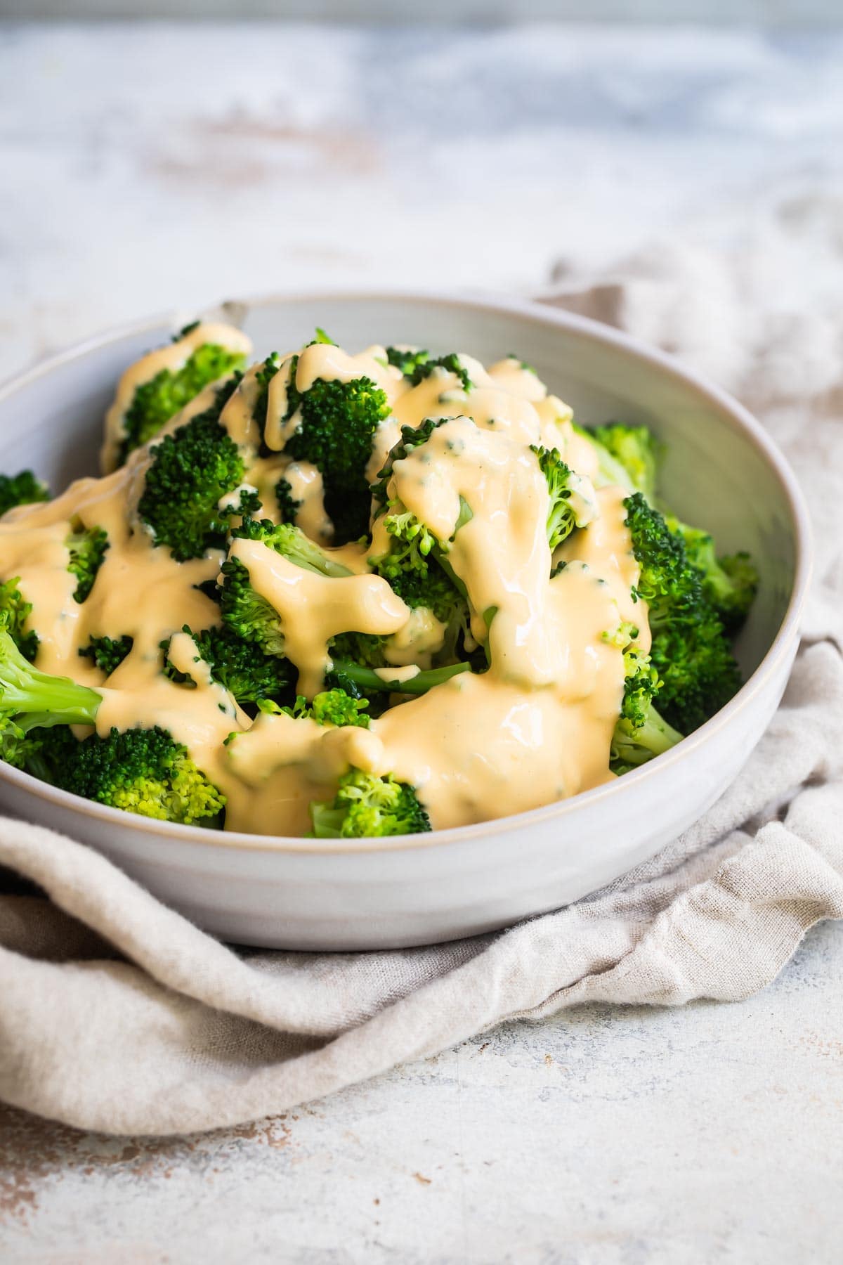 A bowl of blanched broccoli with cheese sauce drizzled on top.