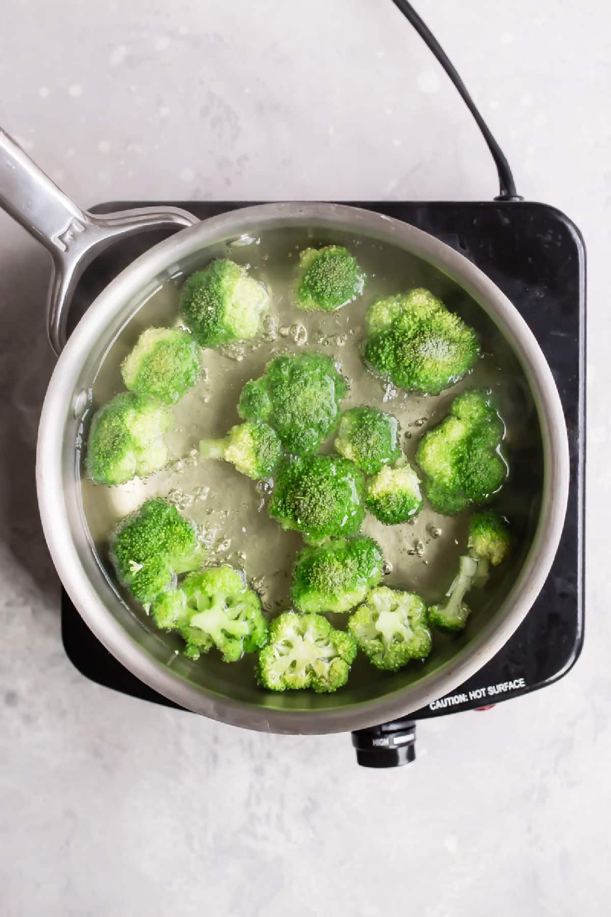 Broccoli cooking in boiling water in a silver pot.