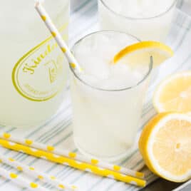 Lemonade in glasses on a silver platter with yellow and white straws and lemon garnish.
