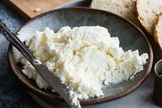 Homemade ricotta cheese in a blue bowl with a knife resting along the side.