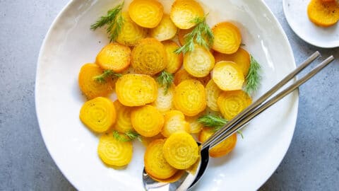 A platter of roasted golden beets, sliced and dressed with vinaigrette and fresh dill fronds.