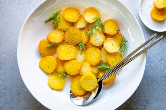A platter of roasted golden beets, sliced and dressed with vinaigrette and fresh dill fronds.