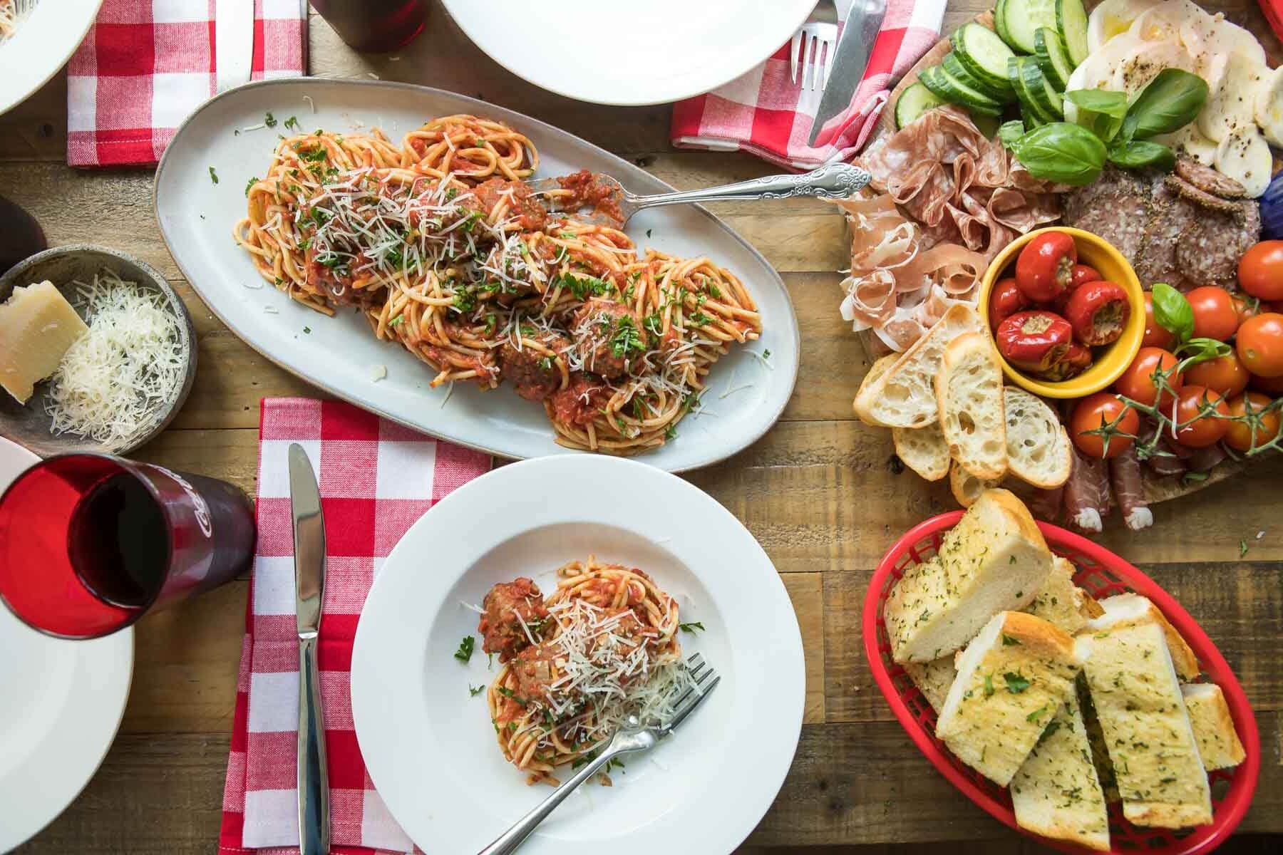Spaghetti and meatballs on a platter surrounded by other Italian food on a table.
