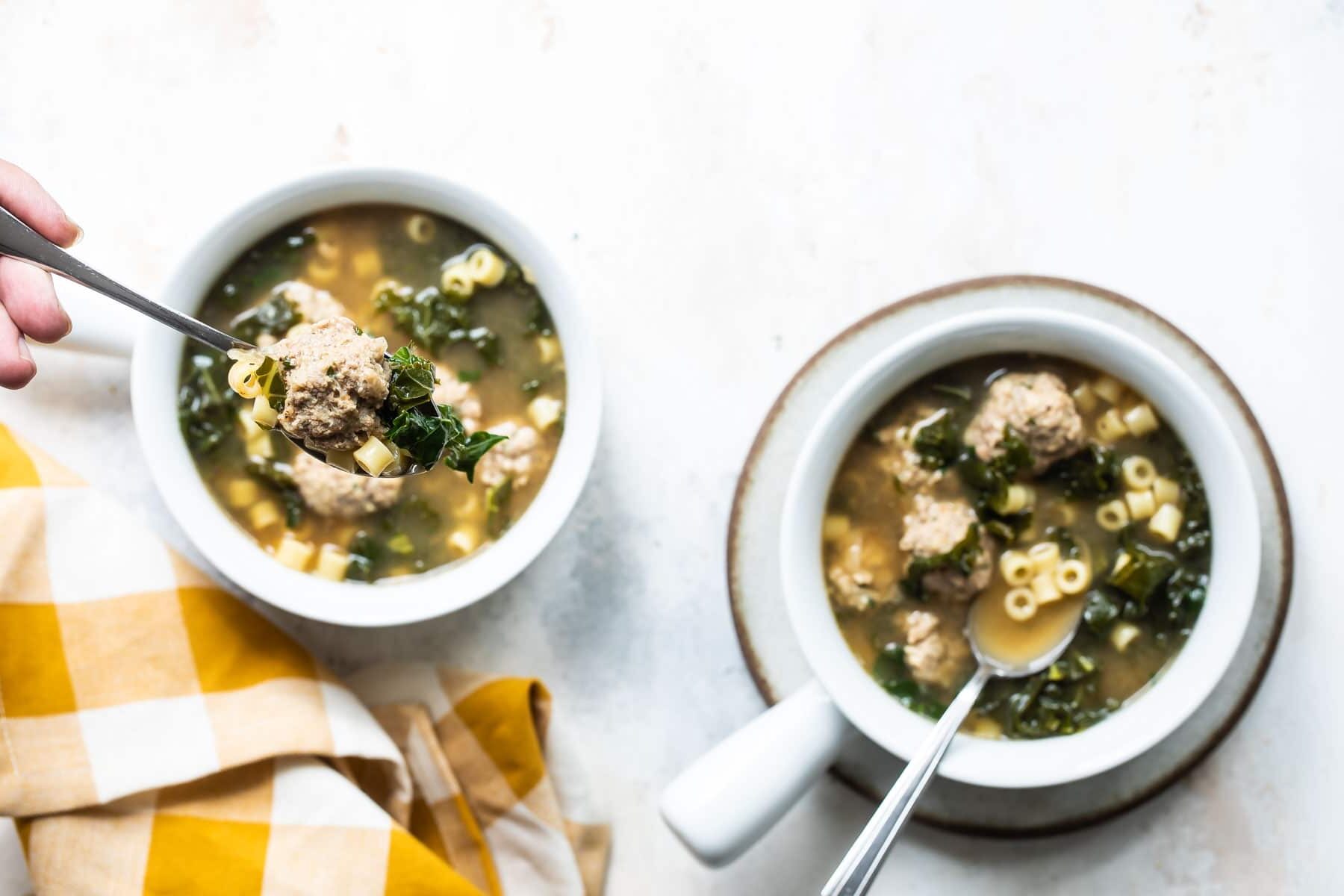 Italian wedding soup being spooned out of a white bowl.