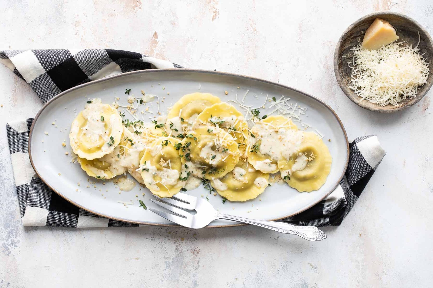 A plate of mushroom ravioli with a small bowl of parmesan cheese.