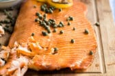 Smoked salmon on a wooden board with capers and lemon slices on top.