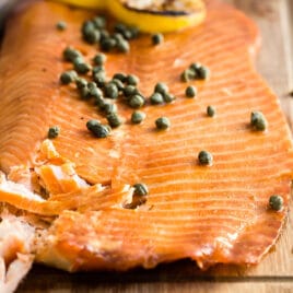 Smoked salmon on a wooden board with capers and lemon slices on top.