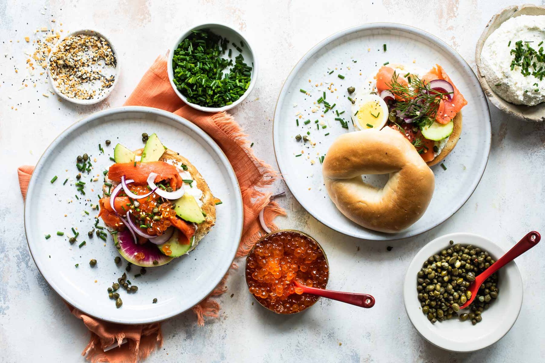 A bagel topped with smoked salmon, salmon roe, avocado, caviar, herbs, and vegetables.